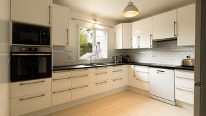 Een moderne keuken met witte kasten, een inbouwoven, een vaatwasser en een raam dat natuurlijk licht binnenlaat.