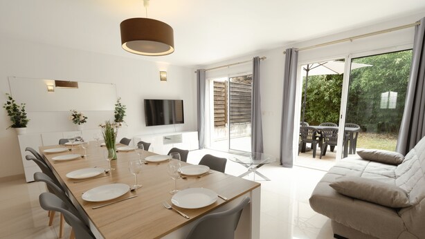 Een moderne eetruimte met een houten tafel gedekt voor zes personen, een bank en een aan de muur bevestigde televisie.
