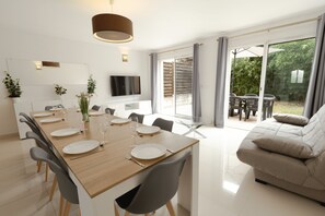 A modern dining area with a wooden table set for six, a sofa, and a TV mounted on the wall. - Cosy house with garden Paris Disney (Bry-sur-Marne)