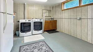 A laundry room with two washing machines, a wooden cabinet, a sink, and a window with a view.