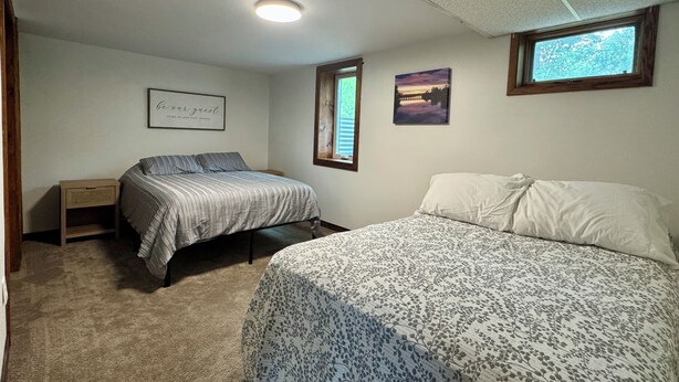 A bedroom with two beds, a nightstand, a ceiling light, and a window.