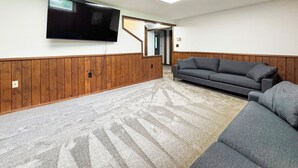 A room with a flat-screen TV mounted on the wall, a gray sofa, and a wooden panel wall.