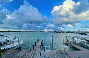 A marina with boats docked, a wooden pier, and a clear sky with clouds. - Livin’ The Dream with 30’ private dock and stunning open water views. (Key Colony Beach)