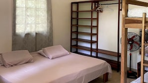 A bedroom with a bed, a wooden wardrobe, a fan, and a window with curtains. - luna caribena (Cahuita)