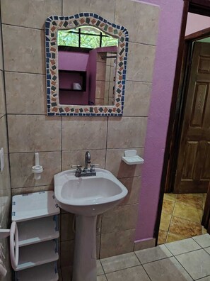 Un baño con lavamanos blanco, espejo con marco de mosaico y pared morada.