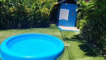A blue inflatable pool surrounded by lush greenery and a small blue shed with a sign.