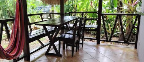 Une terrasse extérieure couverte, dotée d’une table et de chaises, entourée d’une balustrade et d’une végétation luxuriante.