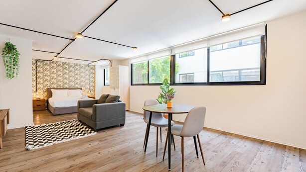 A modern living room with a sofa, a dining table with chairs, a patterned rug, and a large window with a view of greenery. - VH | Loft Condesa with great concierge service | 253 (Ciudad de México)