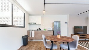 A modern kitchen with white cabinets, a wooden dining table with two chairs, and a black trash bin. - VH | Loft Condesa with great concierge service | 253 (Ciudad de México)