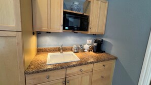 A kitchen with wooden cabinets, a granite countertop, a sink, a microwave, a coffee maker, and a decorative vase.