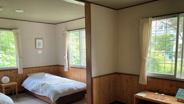 Ein Zimmer mit einem Bett, einem Nachttisch aus Holz, einem Schreibtisch mit Stuhl und einem fenster mit Vorhängen.