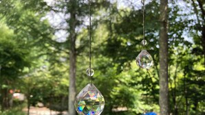 Ein klarer, facettierter Kristallornament hängt im Freien, umgeben von Grünpflanzen.