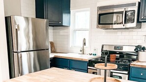 A modern kitchen with a stainless steel refrigerator, a microwave, a stove, and a wooden island with stools. - Hideaway Cabin. Relax and Enjoy (Manistee)