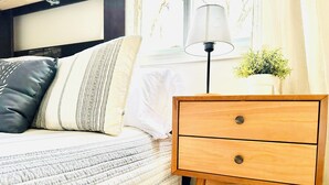 A neatly made bed with patterned pillows, a wooden bedside table with two drawers, a floor lamp, and a small potted plant. - Hideaway Cabin. Relax and Enjoy (Manistee)