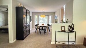 Un vaste espace de vie comprenant une table à manger et des chaises, un meuble noir et une petite table d’appoint agrémentée d’objets décoratifs.