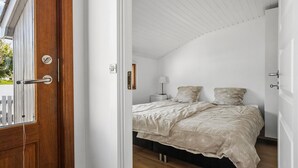 A bedroom with a wooden door, a bed with a floral bedspread, a nightstand with a lamp, and a white ceiling. - Awesome home in Tranekær with WiFi (Tranekær)