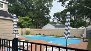 Ein Garten mit Swimmingpool, umgeben von einem Holzzaun, mit zwei Streifen-Sonnenschirmen.