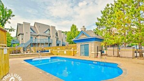 Une piscine entourée de bâtiments, avec une terrasse en bois et un mur en pierre.