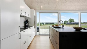 Ett modernt kök med vita skåp, en svart bänkskiva och ett stort fönster som ger utsikt över omgivningen.