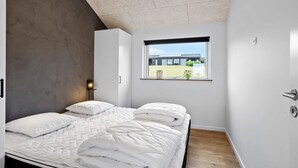 Ett modernt sovrum med en stor säng, ett fönster med utsikt över en byggnad och ett tak med en strukturerad yta.
