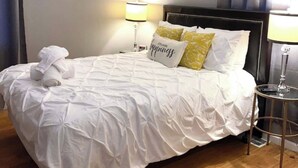 A neatly made bed with a white comforter and pillows, a round table with a lamp, and a ceiling fan. - Charming 1-bedroom apartment with WiFi, AC in marvelous Cincinnati (Cincinnati)