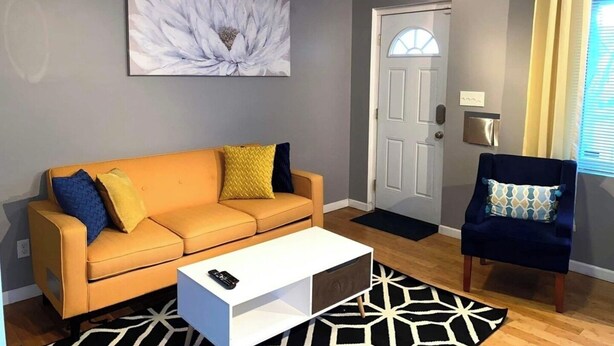 A living room with a sofa, a coffee table, a blue armchair, a door, and a large flower painting on the wall. - Charming 1-bedroom apartment with WiFi, AC in marvelous Cincinnati (Cincinnati)