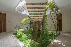 Een ruime atrium met een betegelde trap, weelderig groen en een houten deur.