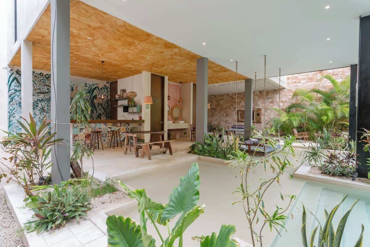 A spacious indoor area with a wooden ceiling, a dining area with tables and chairs, and a variety of plants.