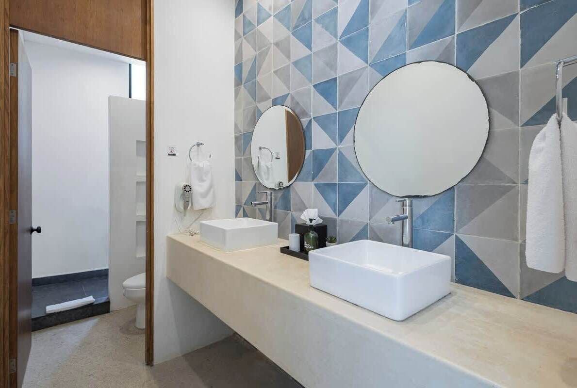 Une salle de bain moderne avec un lavabo blanc, deux miroirs et un mur recouvert de carreaux bleus.