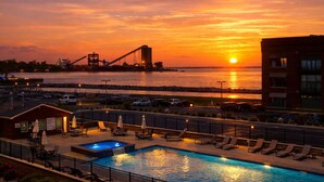 Ein Hotelpoolbereich mit Liegestühlen und Blick auf einen Sonnenuntergang über einer Brücke.