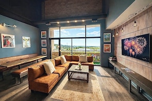 Een moderne woonkamer met een groot raam, een hoekbank, een salontafel en een flatscreen televisie aan de muur.