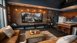 Ein modernes Wohnzimmer mit einem großen Flachbildfernseher, braunen Sofas, einem Couchtisch und einer Küchenzeile mit Barhockern.