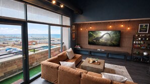 Ein modernes Wohnzimmer mit großem Fenster mit Blick auf eine Marina, einem bequemen Sofa, einem Couchtisch und einem an der Wand befestigten Fernseher.
