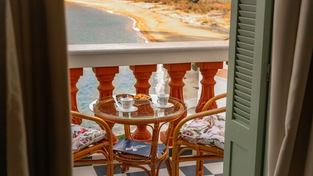 A balcony with wicker chairs, a glass table, and a view of a beach. - A charming retreat with timeless beauty (Andros Chora)