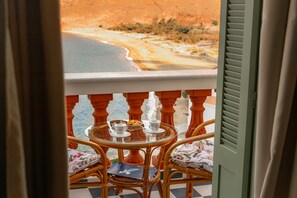 A balcony with wicker chairs, a glass table, and a view of a beach.