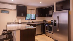 A modern kitchen with dark cabinets, stainless steel appliances, a granite countertop, and a window with a view of greenery. - Ocotal - 2 Full Units - Steps to the Beach (Sardinal)
