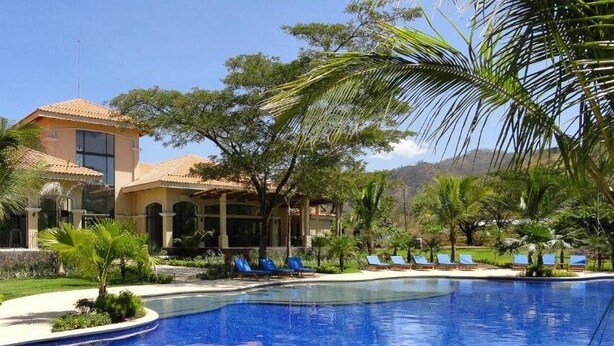 A resort with a swimming pool, palm trees, and a building with a tiled roof. - Ocotal - 2 Full Units - Steps to the Beach (Sardinal)