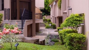 A modern building with a covered outdoor area, steps leading to a door, and a small garden with pink flowers and green shrubs. - Ocotal - 2 Full Units - Steps to the Beach (Sardinal)