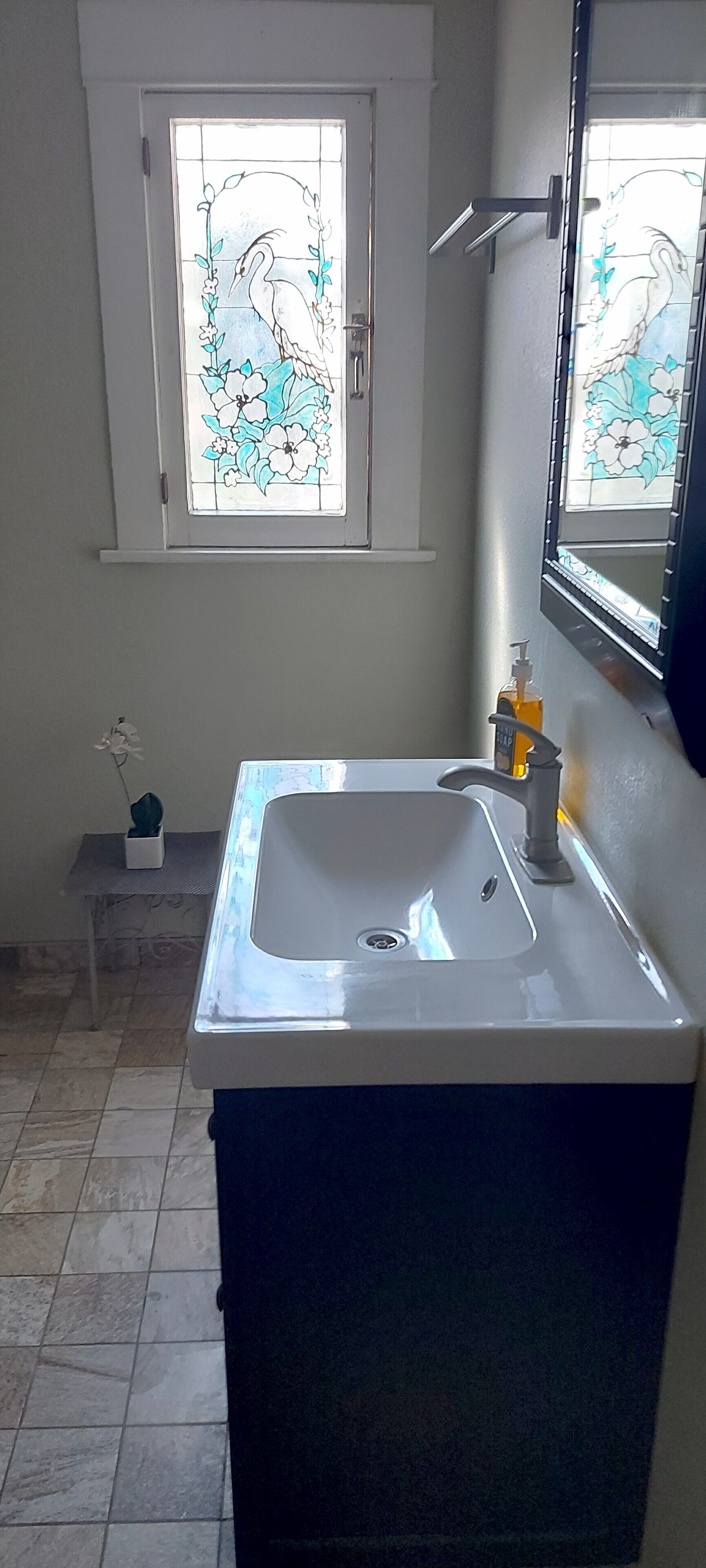 A bathroom with a white sink, a mirror, and a window with a floral design.