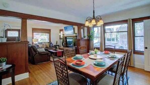Amplia sala de estar con una mesa de comedor de madera preparada para cuatro personas, una chimenea y un gran ventanal con cortinas.