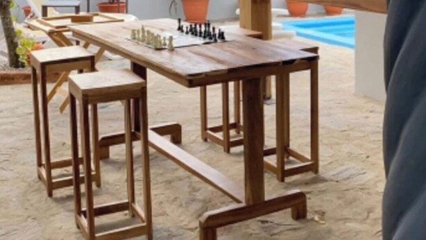 Una terraza de madera al aire libre con una mesa y sillas, rodeada de plantas en macetas y una piscina.
