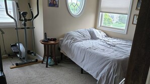 Una camera da letto con un letto, un'attrezzatura per esercizi, un tavolino con un telefono e una finestra con persiane.