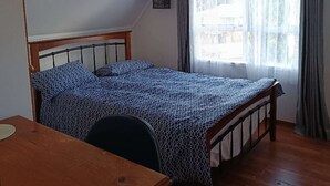 A bedroom with a wooden bed, a desk, a hanging light, and a window with curtains. - Cosy and Budget room in a vintage house located at Northshore, Auckland (Auckland)