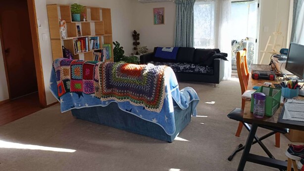 A cozy living room with a large blue couch, a bookshelf filled with books, and a wooden coffee table. - Cosy and Budget room in a vintage house located at Northshore, Auckland (Auckland)