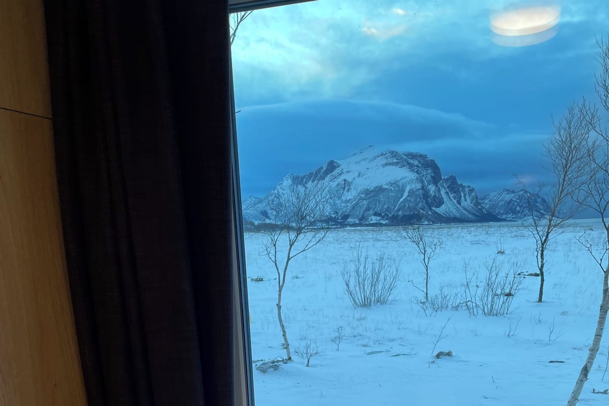Een kamer met een raam dat uitkijkt op een besneeuwd landschap met bergen.