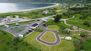Vue aérienne d’un terrain de camping avec des emplacements pour camping-cars, un petit bâtiment et une route menant à une plage.