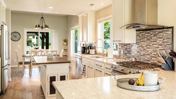 A modern kitchen with a large island, stainless steel appliances, and a brick backsplash.