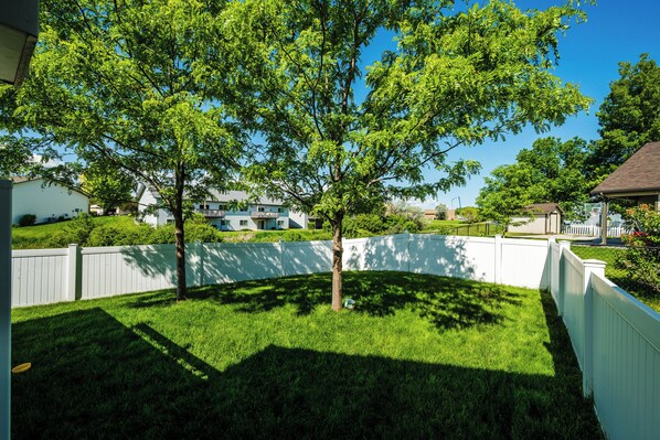 A residential backyard with a white fence, a tree, and houses in the background.