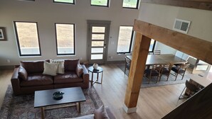 Amplia sala de estar con un sofá de cuero marrón, una mesa de centro y un comedor con una mesa y sillas de madera.