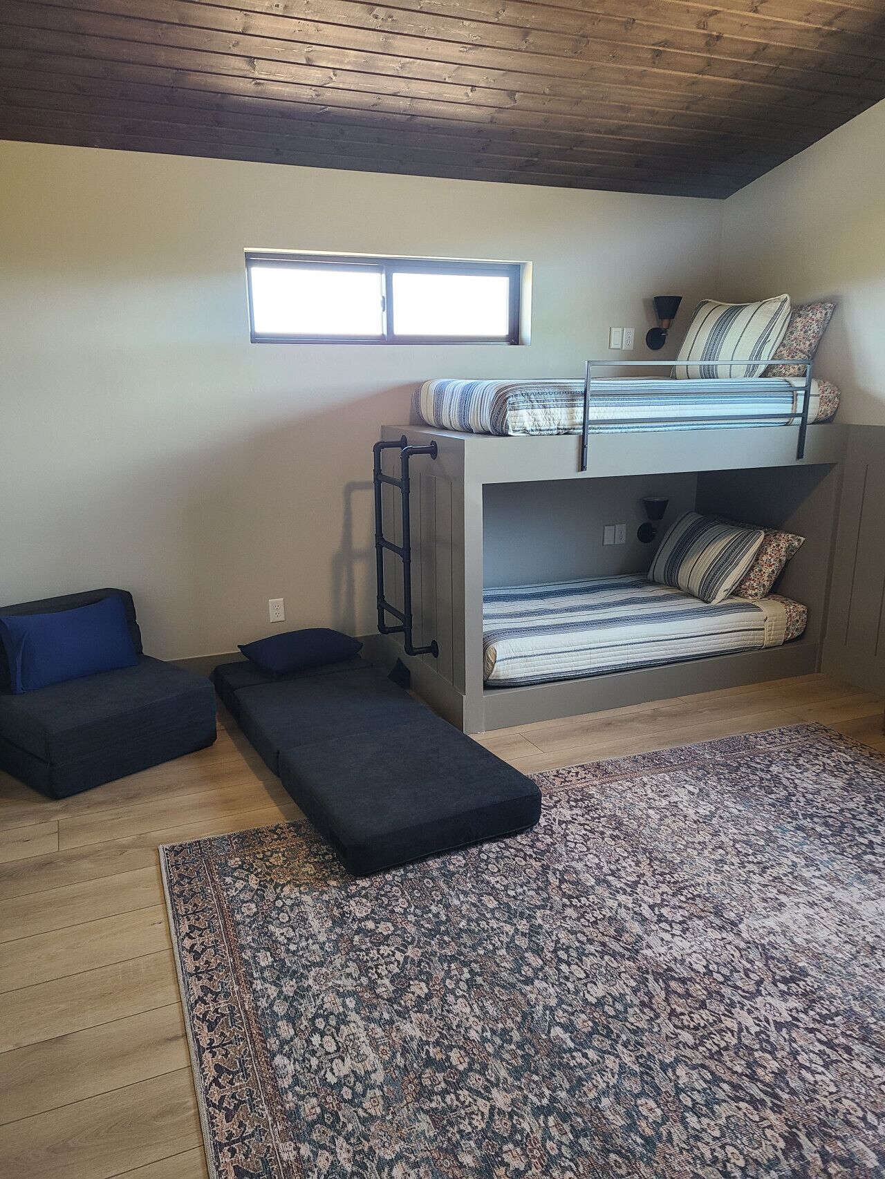 A compact room with a bunk bed, a small sofa, a bench, and a patterned rug.